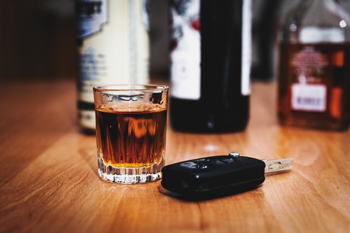 Car keys next to liquor bottles and glass of alcohol