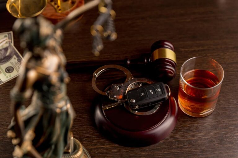 DUI hearing represented by a glass of liquor, car keys, a gavel, and a statue of Lady Justice on a courtroom table.