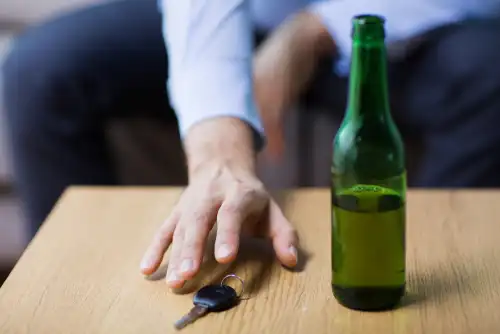 man reaching for car keys next to beer bottle
